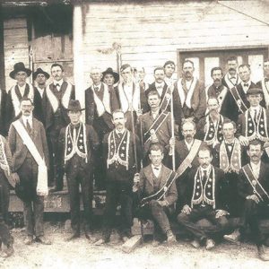 Group of white men in hats and suits with Masonic garb outside building