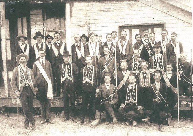 Group of white men in hats and suits with Masonic garb outside building