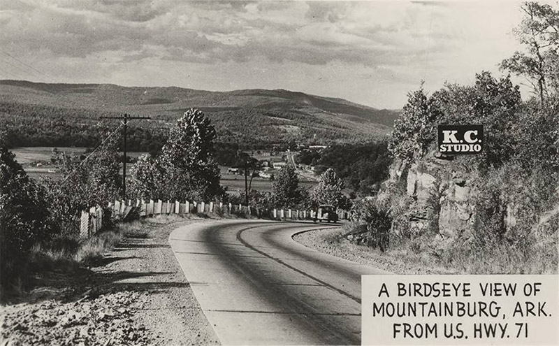 Mountain road with town and countryside in the background from "K. C. Studio" labeled "A Birds eye view of Mountainburg Arkansas from U.S. Highway 71"