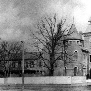 Two-story convent building with towers and wall on street corner with bare trees