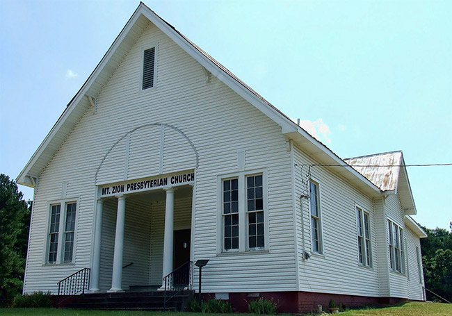 Single-story building with white wood siding and steeple roof and columned entry way