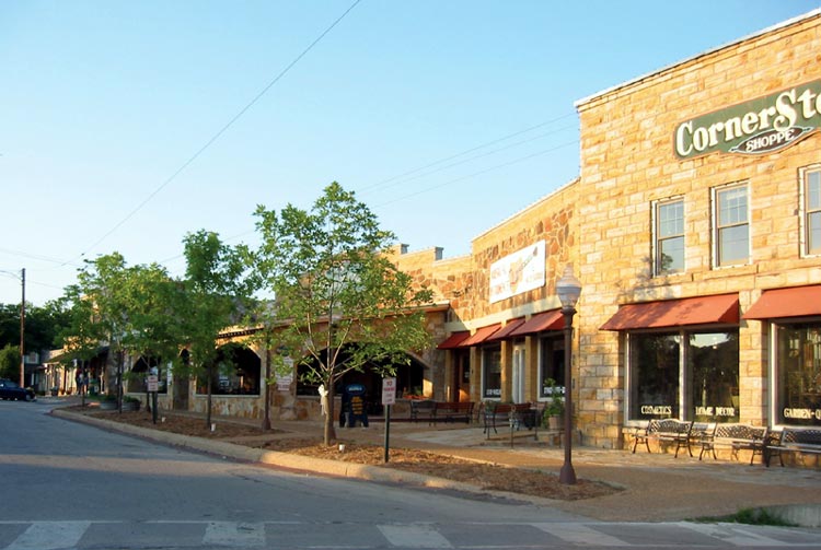 Town street with brick and stone storefronts and lighting fixtures, trees