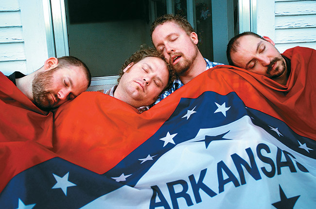 Four white men sleeping under Arkansas flag blanket