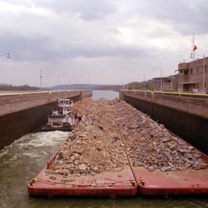 Barges covered in rocks and a tugboat passing through a lock