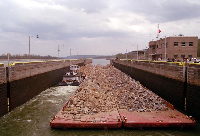 Barges covered in rocks and a tugboat passing through a lock
