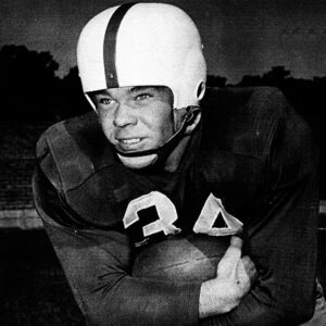 White man in football uniform and helmet holding a football