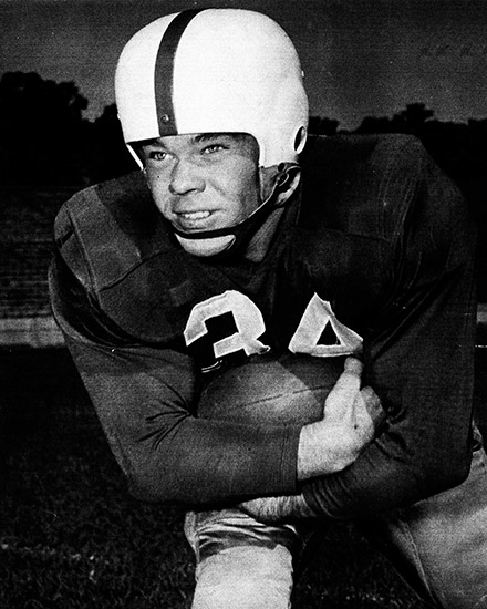 White man in football uniform and helmet holding a football