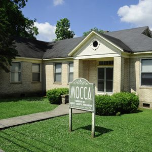 Single-story house with "M.O.C.C.A." sign and yard