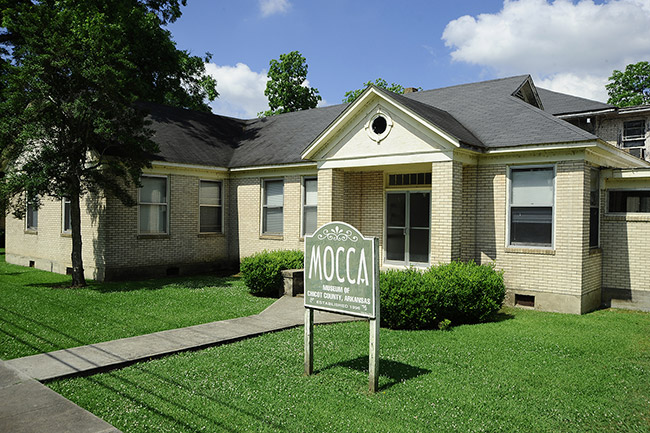 Single-story house with "M.O.C.C.A." sign and yard
