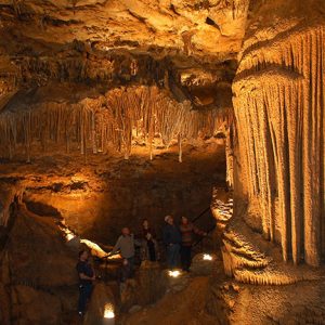 White tourists marveling inside deep cave with stalactites