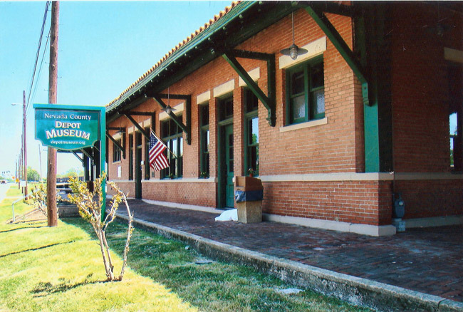 Close-up of single-story brick building with sidewalk and hanging sign on grass