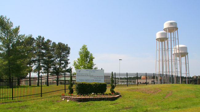 sign outside fence with three water towers and buildings in background