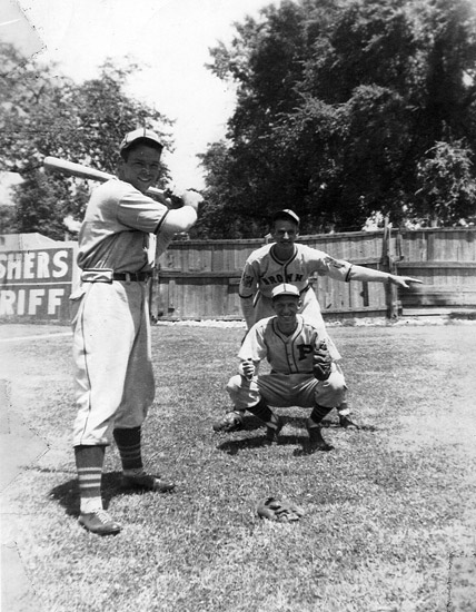 Young white catcher umpire and batter in uniforms playing baseball with wooden fence behind them