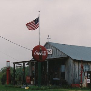 Single-story storefront with covered porch flag pole and Coca-Cola sign on grass