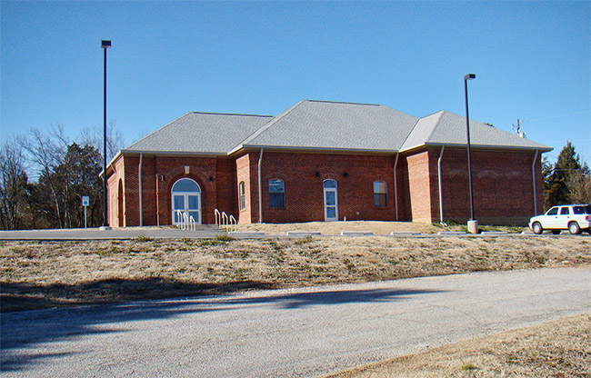 Single-story brick building with arched windows and parking lot