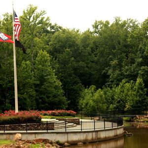 American and Arkansas flags on flagpoles near pond and trees