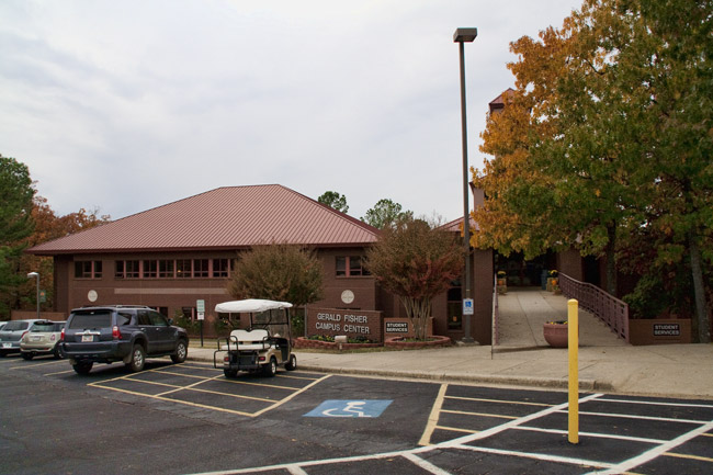 Brick building with red roof and tower and parking lot with cars and a golf card