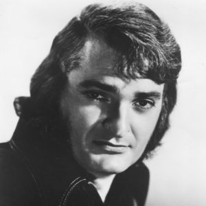 White man with dark eyes and wavy hair in collared shirt