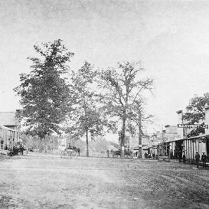 Storefronts on dirt road with trees and horses in the background