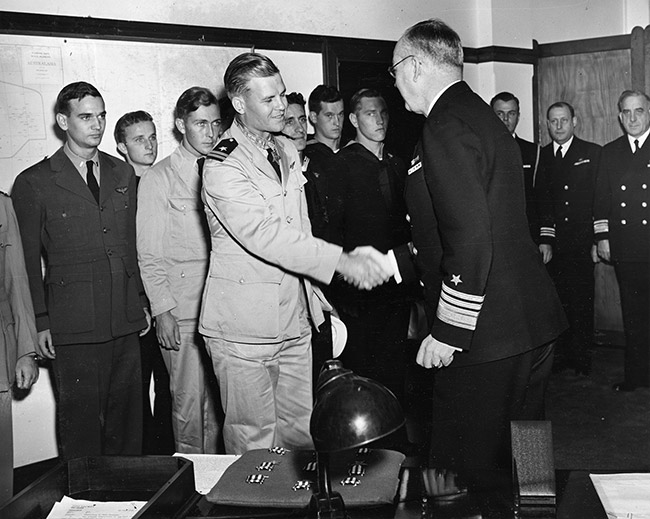 Young white men in military uniform with one of them shaking hands with older white officer