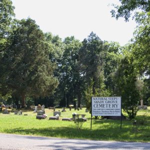 Sunny street with cemetery and white sign and trees