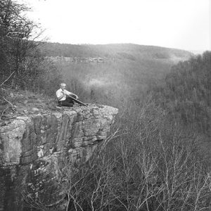 Old white man sitting on cliff overlooking tree covered valley
