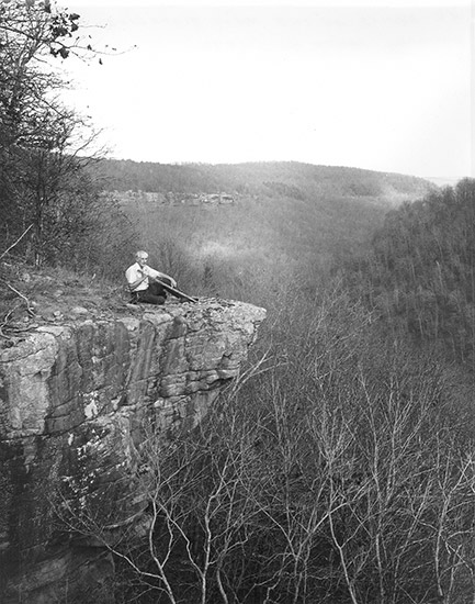 Old white man sitting on cliff overlooking tree covered valley
