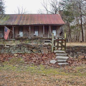 Wood cabin with rusted metal roof and stone wall with gate and American flag