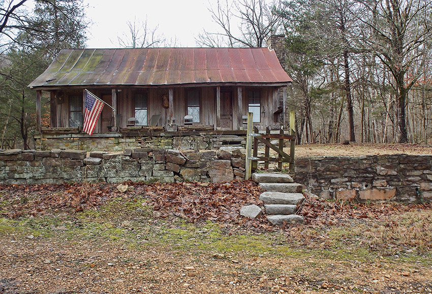 Wood cabin with rusted metal roof and stone wall with gate and American flag