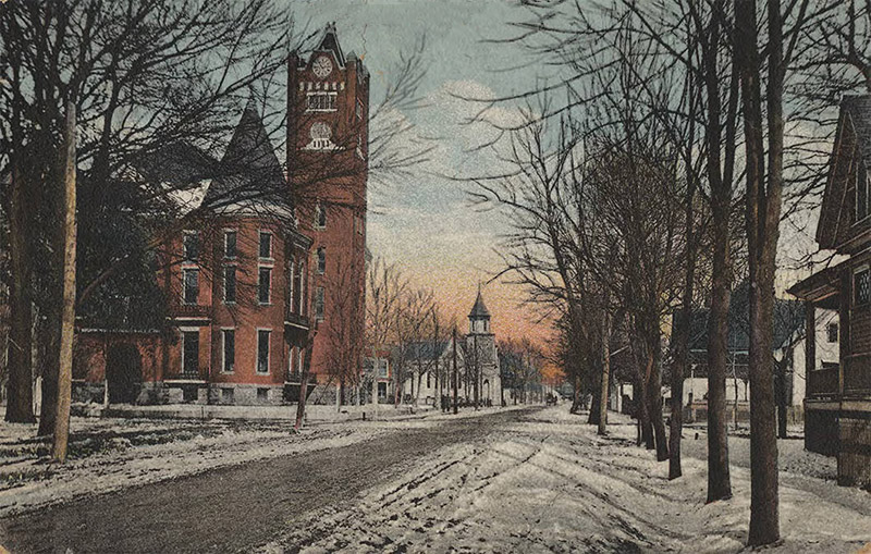 Multistory building with clock tower and multistory building with bell tower across from houses on town street in winter
