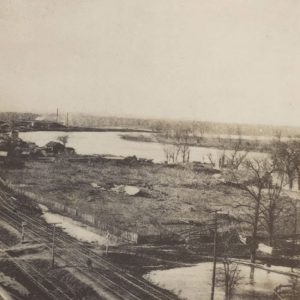 Railroad tracks, trees, water, seen from elevated spot
