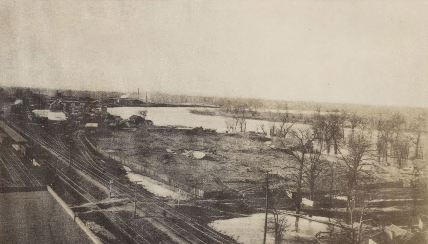 Railroad tracks, trees, water, seen from elevated spot