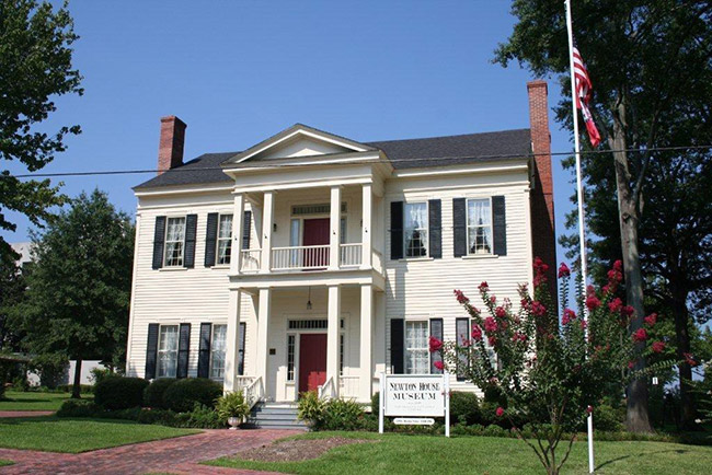 Multistory house with covered porch and balcony with sign and flagpole in the front yard
