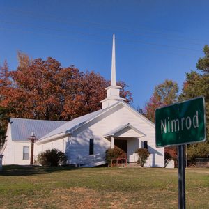 Single-story building with covered porch and steeple with "Nimrod" road sign in the foreground