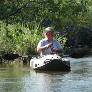 Old white man wearing a straw hat fishing in a kayak