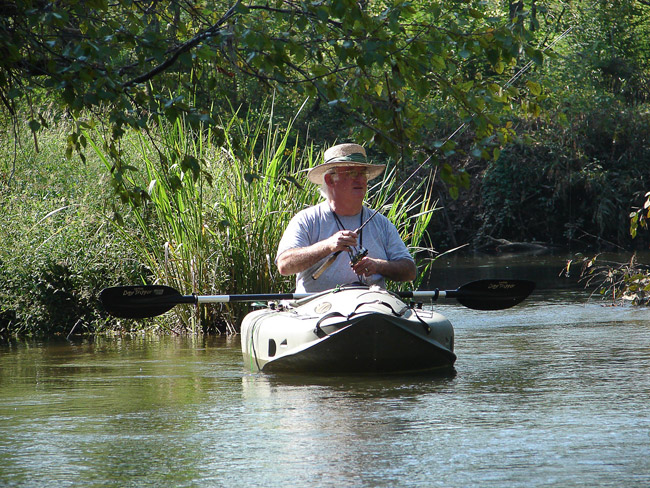 Old white man wearing a straw hat fishing in a kayak