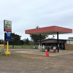 Single-story gas and grocery store with red canopy and signs on gravel parking lot