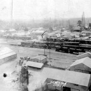 Aerial view of rail yard and factory buildings with oil derrick in the background