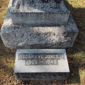 "Oscar Eve Jones II" flat gravestone in front of monument in cemetery