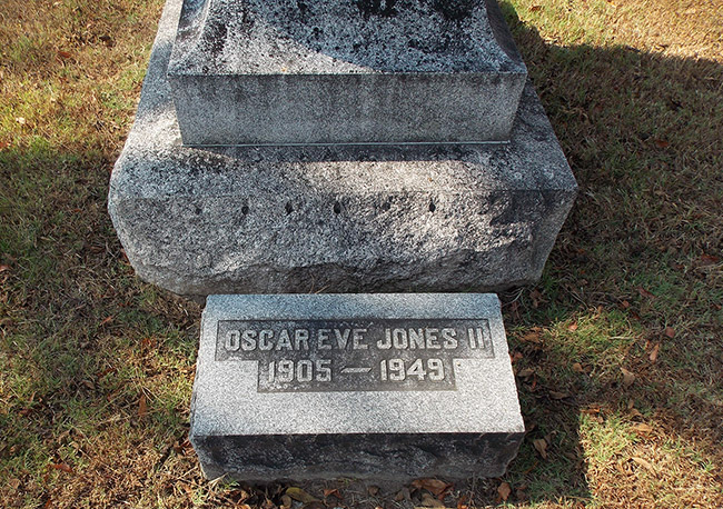 "Oscar Eve Jones II" flat gravestone in front of monument in cemetery