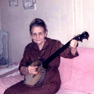 Older white woman in maroon checkered dress playing a banjo