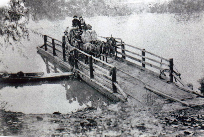 White couple on horse drawn wagon and white ferrymen landing ferry on river shore