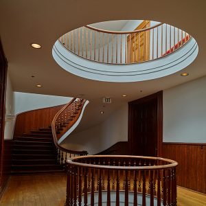 Rotunda opening with circular wooden hand railing and another rotunda opening above it with curved staircase in the background