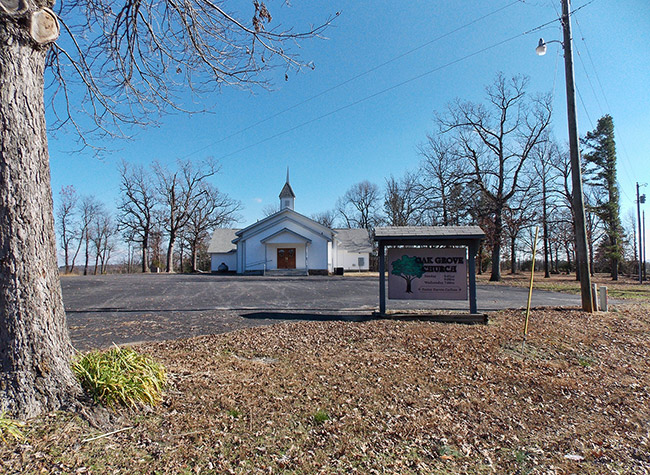 Single-story building with cupola and covered porch on parking lot with sign in the foreground