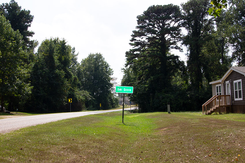 Single-story house with "Oak Grove" road sign in its front yard by rural road