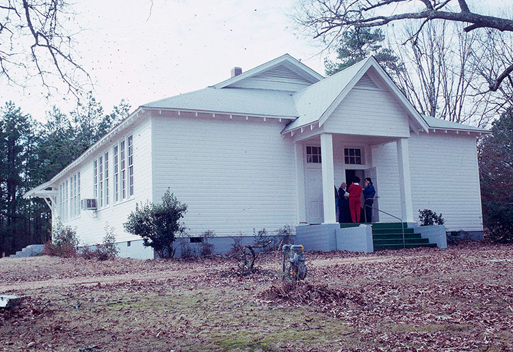 People entering a single-story building with white siding