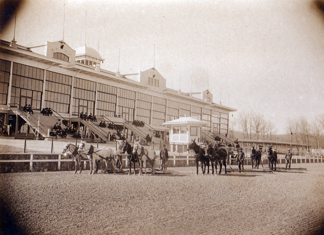 Race horses and men on track next to stands