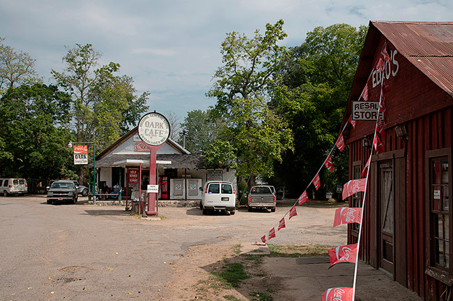 Storefront and cafe on dirt road with parked cars