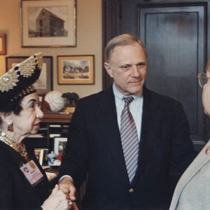 Older white woman speaking with two older white men in suits