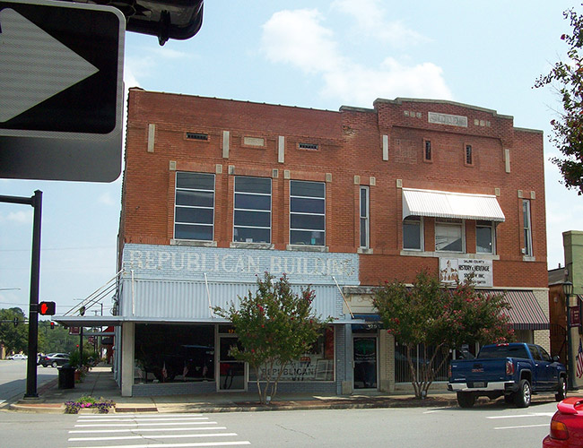 Multistory brick building with trees and parked truck on town street